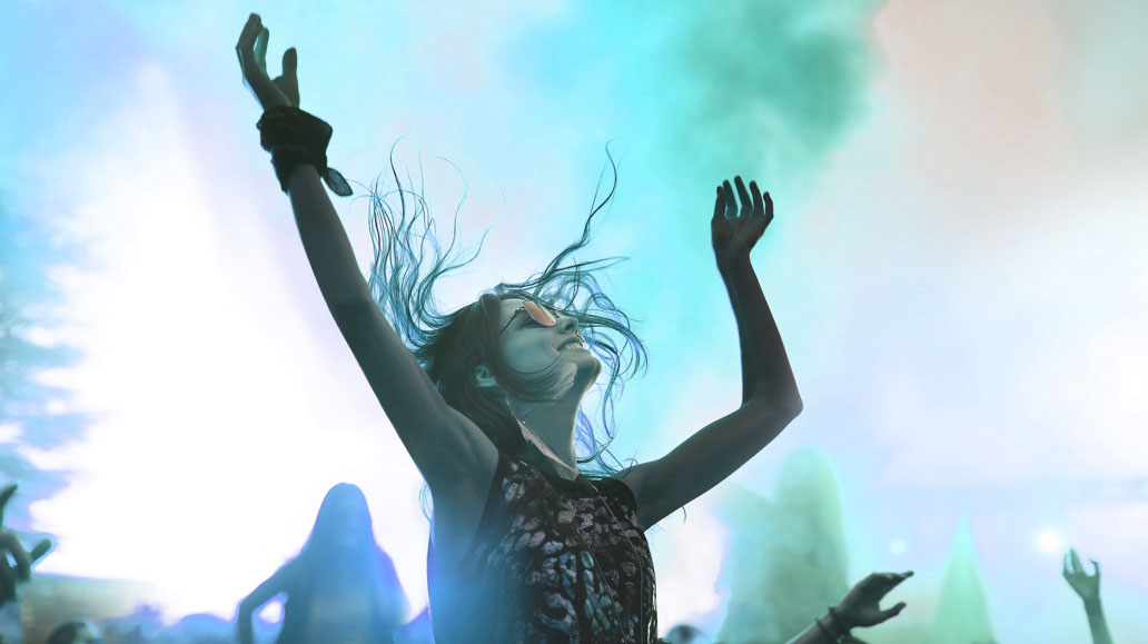 A woman with raised arms dances in the smoke at a Bees Knees concert.